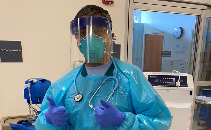 A UNC physician gives two thumbs up to the camera. He is wearing a mask, face shield, protective gown, and gloves. His eyes look tired, but hopeful.